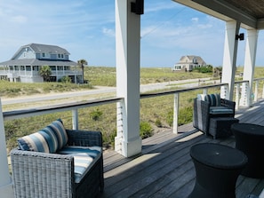 Ein überdachter Außenbereich mit Korbmöbeln, Blick auf den Strand und ein Haus im Hintergrund.