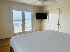 Une chambre à coucher avec un lit, un téléviseur fixé au mur et une porte-fenêtre coulissante donnant sur un balcon.