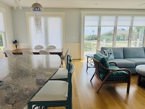 A spacious living area with a dining table, chairs, a sofa, and a view through large windows. - Ocean Views & Southern Charm on Bald Head Island (Bald Head Island)