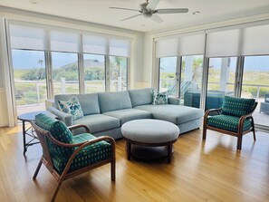 A modern living room with a sectional sofa, two armchairs, a coffee table, and large windows offering a view of the outdoors. - Ocean Views & Southern Charm on Bald Head Island (Bald Head Island)