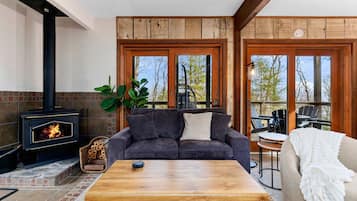 Una sala de estar acogedora con chimenea, un sofá, una mesa de centro y vistas amplias a través de ventanas grandes.