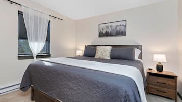 A bedroom with a bed, bedside tables, a window with sheer curtains, and a wall-mounted painting.