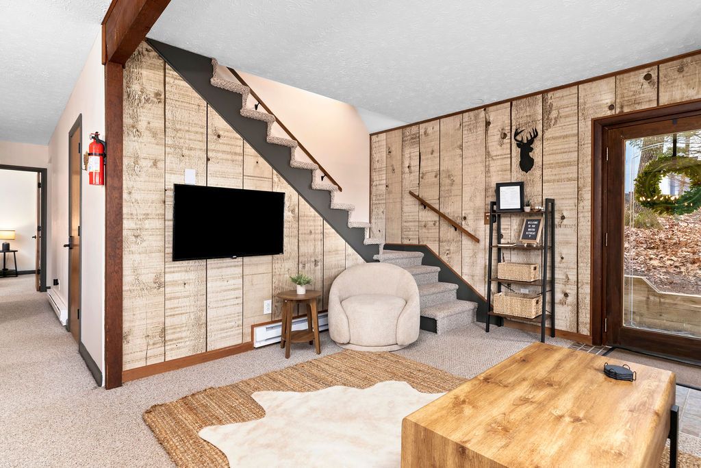 A living room with a wooden wall, a mounted TV, a staircase, a white armchair, and a wooden coffee table.