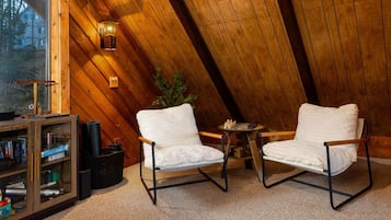 A cozy room with wooden walls, a bookshelf, two white cushioned chairs, a small table, and a lamp.