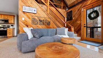 Ein gemütliches Wohnzimmer mit einer Eckcouch, Holzelementen und einem Schild mit der Aufschrift 'SKI LODGE'.
