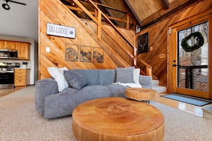 Una sala de estar acogedora con un sofá seccional, detalles de madera y un letrero que dice 'SKI LODGE'.