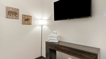 A room with a flat-screen TV mounted on the wall, a standing floor lamp, and two wooden wall art pieces.