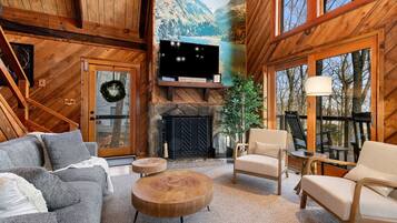 A cozy living room with a fireplace, comfortable seating, and a large window overlooking a mountainous landscape.