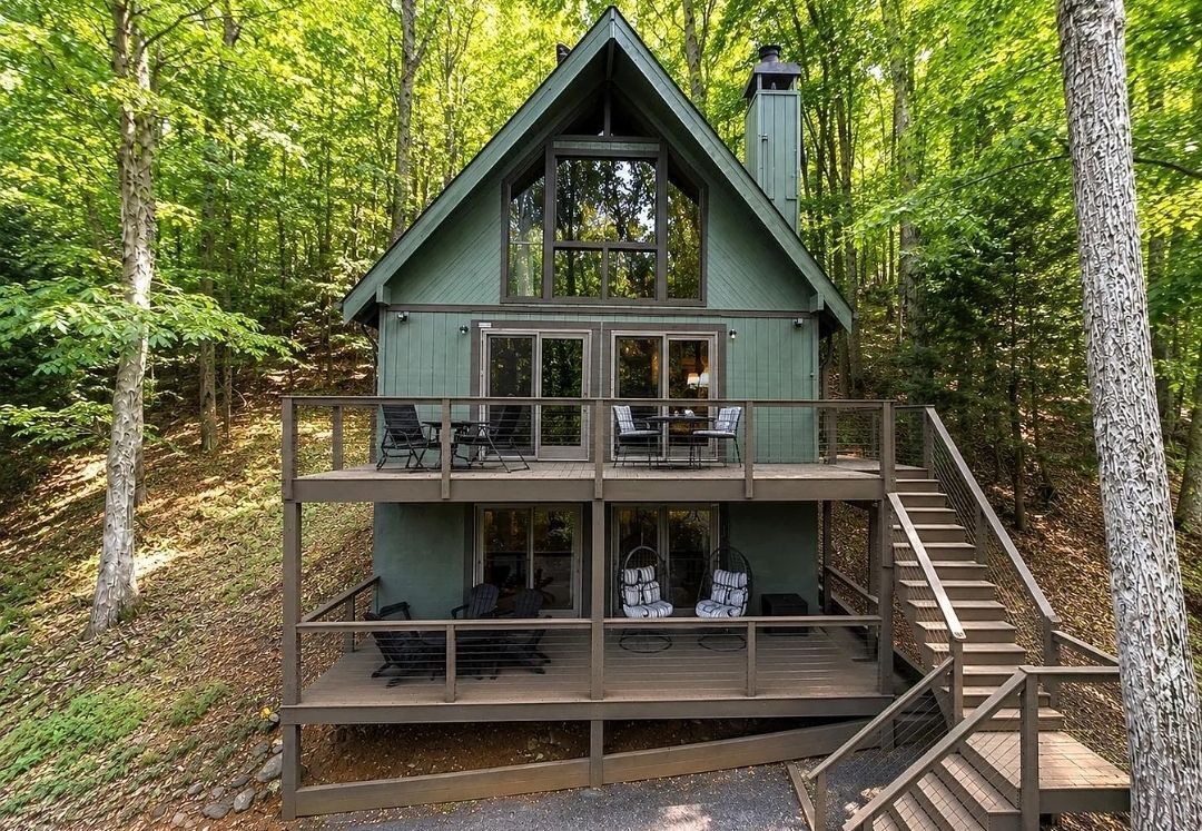 A two-story cabin with a balcony, surrounded by trees.