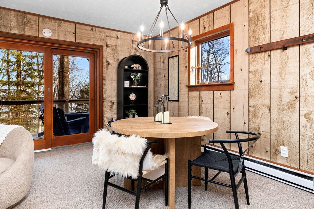 Ein Zimmer mit Holzwänden, einem runden Holztisch, zwei Stühlen, einer Kristallleuchtre und einem großen Fenster.