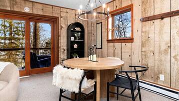 Ein Zimmer mit Holzwänden, einem runden Holztisch, zwei Stühlen, einer Kristallleuchtre und einem großen Fenster.
