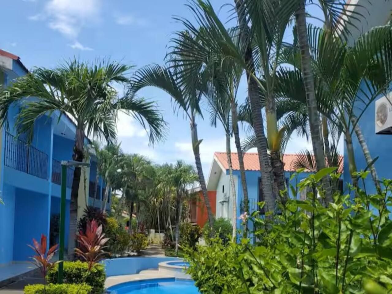 A resort courtyard with palm trees, a swimming pool, and colorful buildings.