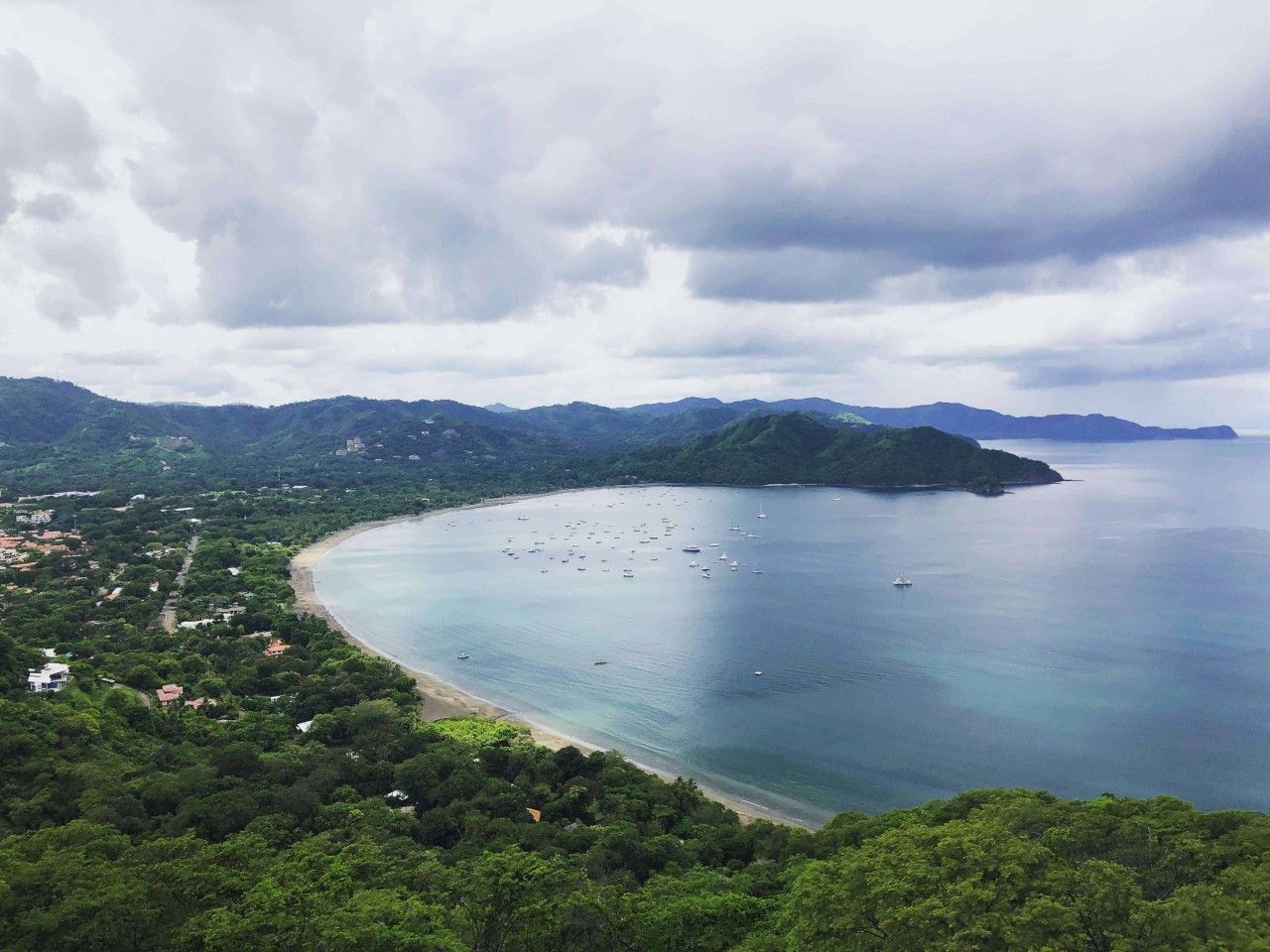 A coastal landscape with a beach, boats, and a mountainous backdrop.