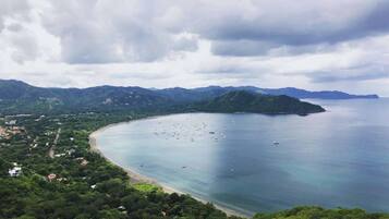 A coastal landscape with a beach, boats, and a mountainous backdrop.