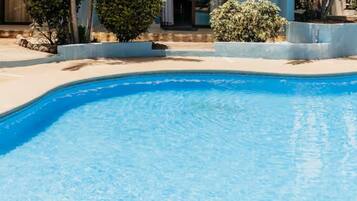 A swimming pool with a curved edge, surrounded by a concrete deck and small bushes.