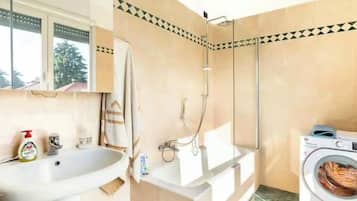 Un baño con lavamanos, espejo, toallero, ducha y lavadora.