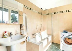 A bathroom with a sink, mirror, towel rack, shower, and a washing machine. - Lodi Apartment (Lodi)