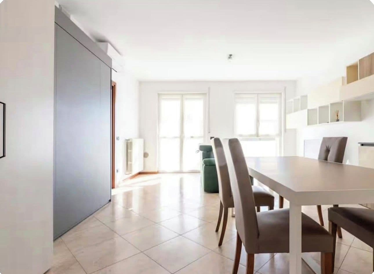 Zona pranzo moderna con un tavolo grande e sedie, un mobile contenitore grigio e vista all'esterno tramite ampie finestre.