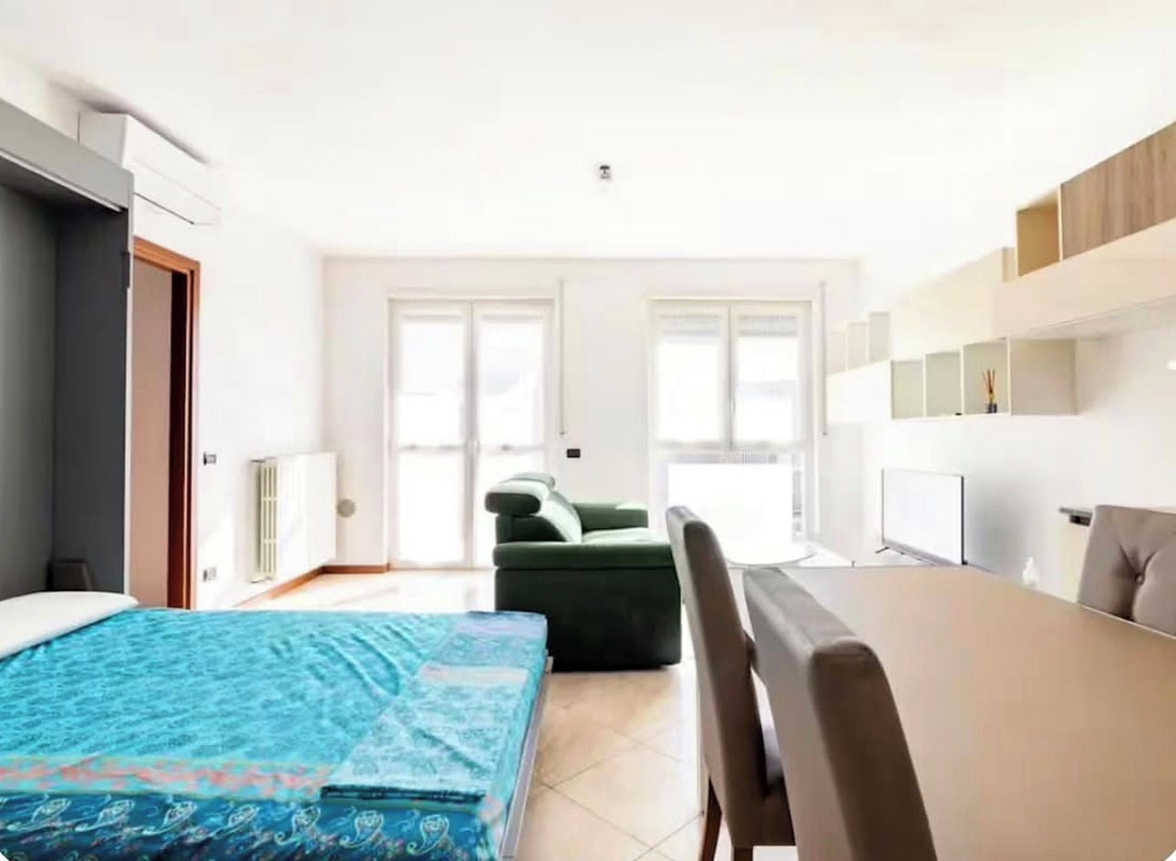 Una habitación de hotel moderna con una cama, un sofá verde, una mesa de comedor y una kitchenette.