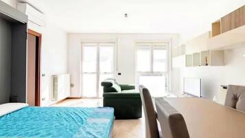 Una habitación de hotel moderna con una cama, un sofá verde, una mesa de comedor y una kitchenette.