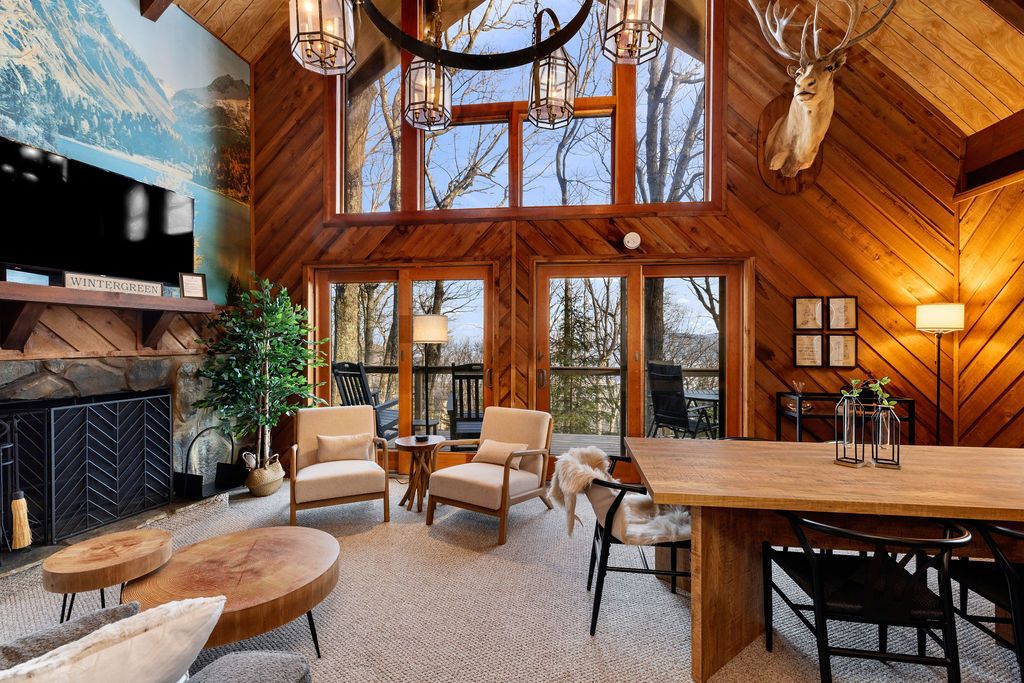 A cozy cabin interior with a fireplace, comfortable seating, and large windows.