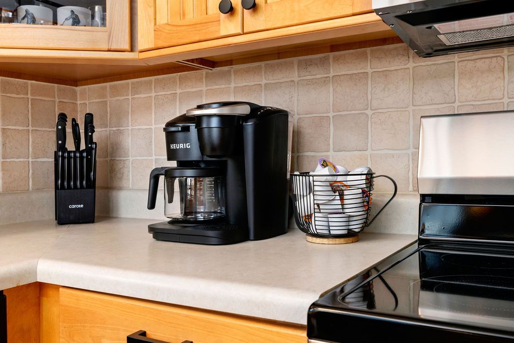 A kitchen with a coffee maker, a knife block, and a basket of items on the counter.