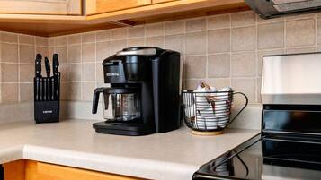 A kitchen with a coffee maker, a knife block, and a basket of items on the counter.