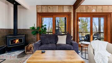 A cozy living room with a fireplace, a sofa, a coffee table, and a view of the outdoors.