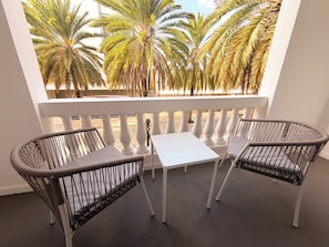 Ein Balkon mit Korbstühlen und einem Tisch, der Blick auf Palmen und einen Strand bietet.