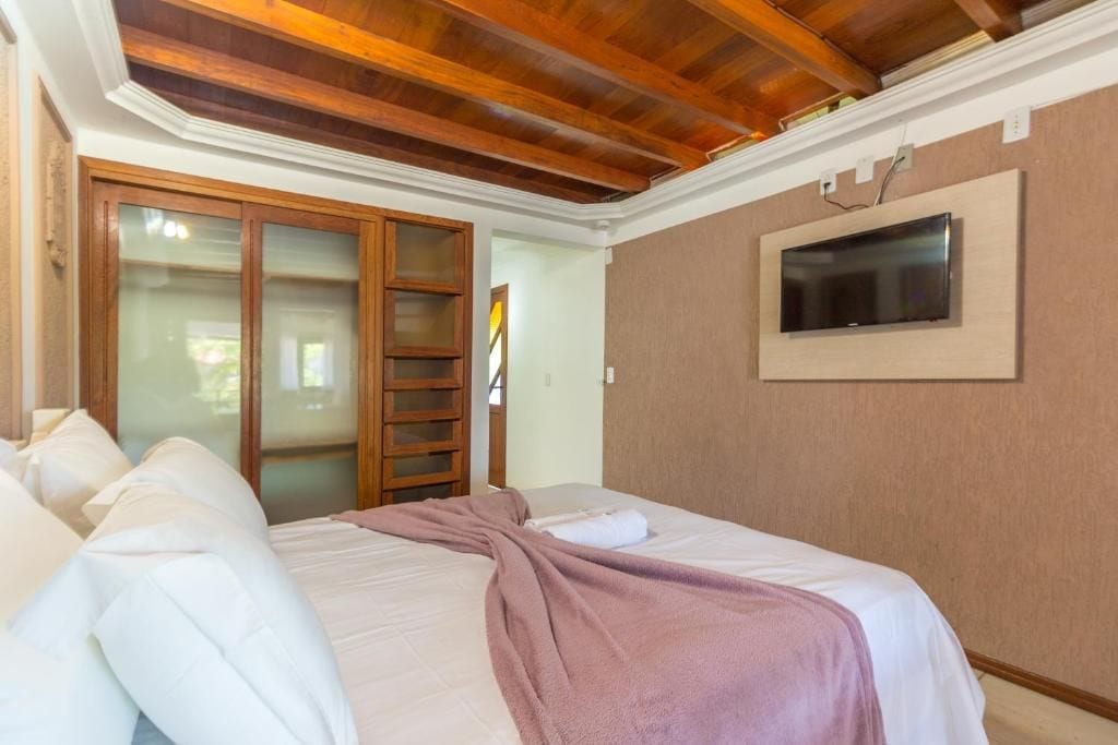 Quarto com cama, televisão presa na parede e guarda-roupa com porta de correr.
