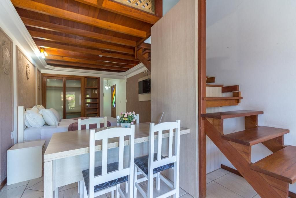 Un comedor con mesa y sillas de madera, una escalera y vista al salón.