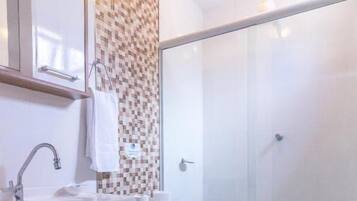A bathroom with a shower, toilet, sink, and a patterned wall.