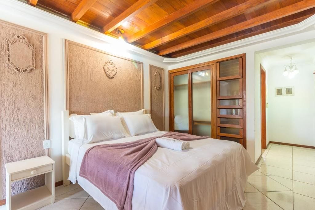A hotel room with a wooden ceiling, a bed with white bedding, a nightstand, and a large window with a view.