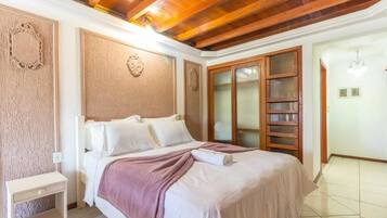 A hotel room with a wooden ceiling, a bed with white bedding, a nightstand, and a large window with a view.