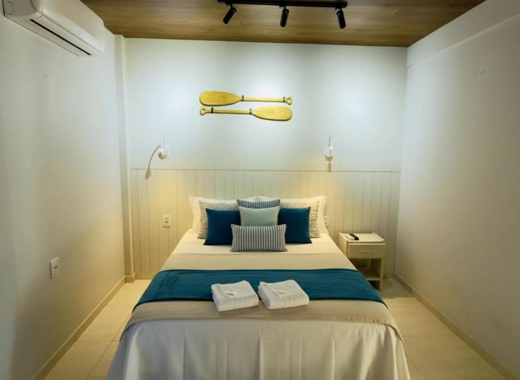 Quarto de hotel com cama, almofadas, mesa de cabeceira e ar condicionado.
