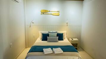 Quarto de hotel com cama, almofadas, mesa de cabeceira e ar condicionado.