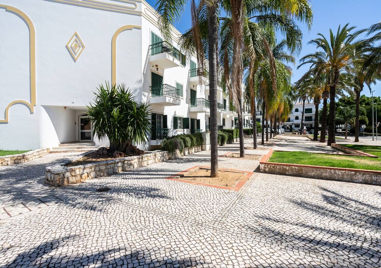 A courtyard with cobblestone flooring, palm trees, and a white building with balconies.
