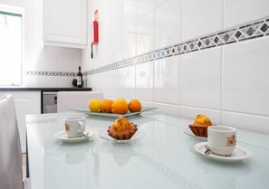 A modern kitchen with white tiles, a glass table, and a fire extinguisher on the wall. - Casa das Chaminés – In Conceicao de Tavira (Tavira)
