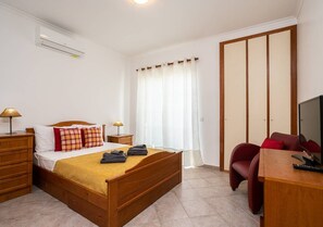 A bedroom with a bed, bedside tables, a TV, a wardrobe, and a window with curtains. - Casa das Chaminés – In Conceicao de Tavira (Tavira)