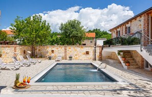 Piscina com espreguiçadeiras e uma saladeira, cercada por muros de pedra e árvores.