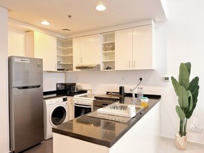A modern kitchen with stainless steel appliances, white cabinetry, and a central island. - Spacious Deluxe 1BR Near Golf Course - POOL - GYM (Dubai)