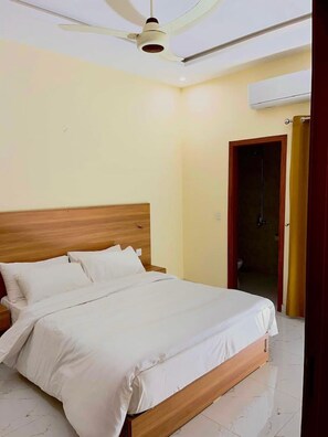 Un dormitorio con cama de madera, ropa de cama blanca, ventilador de techo y equipo de aire acondicionado.