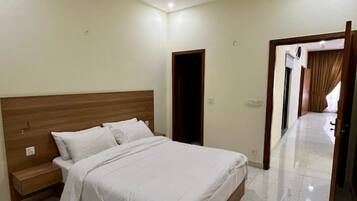 A bedroom with a bed, a nightstand, a ceiling fan, and a door leading to another room.