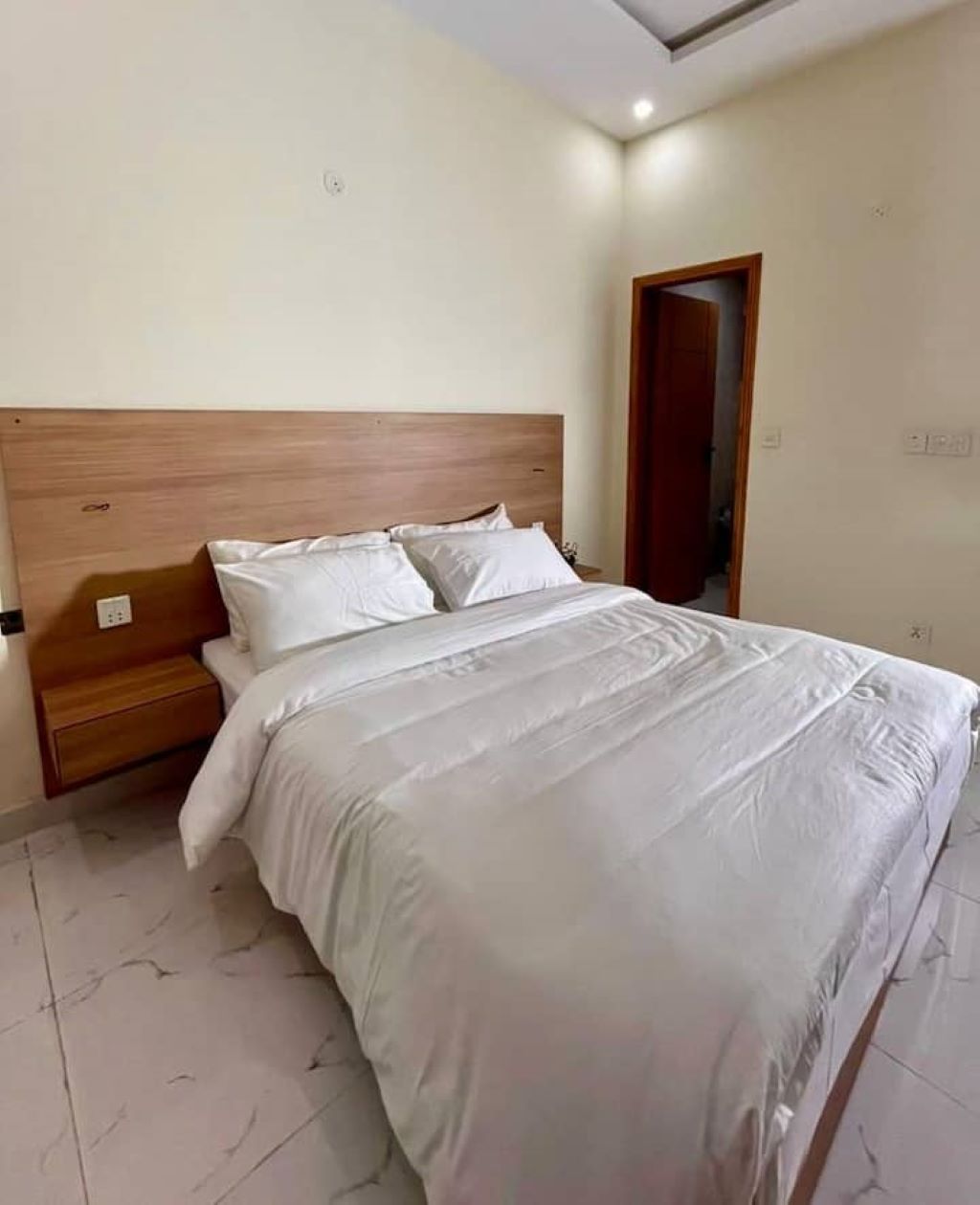 Una cama bien tendida con ropa blanca en una habitación con cabecera de madera y suelo de baldosas.