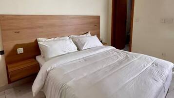 Una cama bien tendida con ropa blanca en una habitación con cabecera de madera y suelo de baldosas.