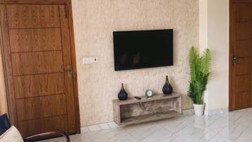 A living room with a flat-screen TV mounted on the wall, a wooden cabinet below, and a round coffee table.