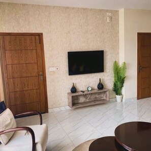 A living room with a flat-screen TV mounted on the wall, a wooden cabinet below, and a round coffee table.