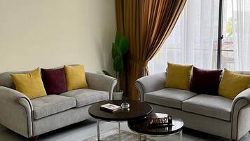 Sala de estar com dois sofás, uma mesa de centro e uma janela grande com cortinas.