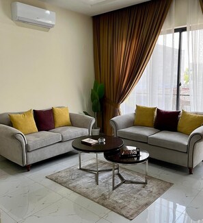 Sala de estar com dois sofás, uma mesa de centro e uma janela grande com cortinas.