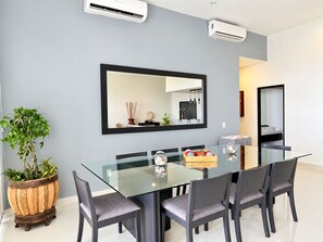 A modern dining area with a glass table, six chairs, a large mirror, and a potted plant. - Beachfront Condo · AMERICAN FESTIVAL ACCESS - Private Jacuzzi · 5 Bedrooms - 5.5 Bathrooms (Las Jarretaderas)